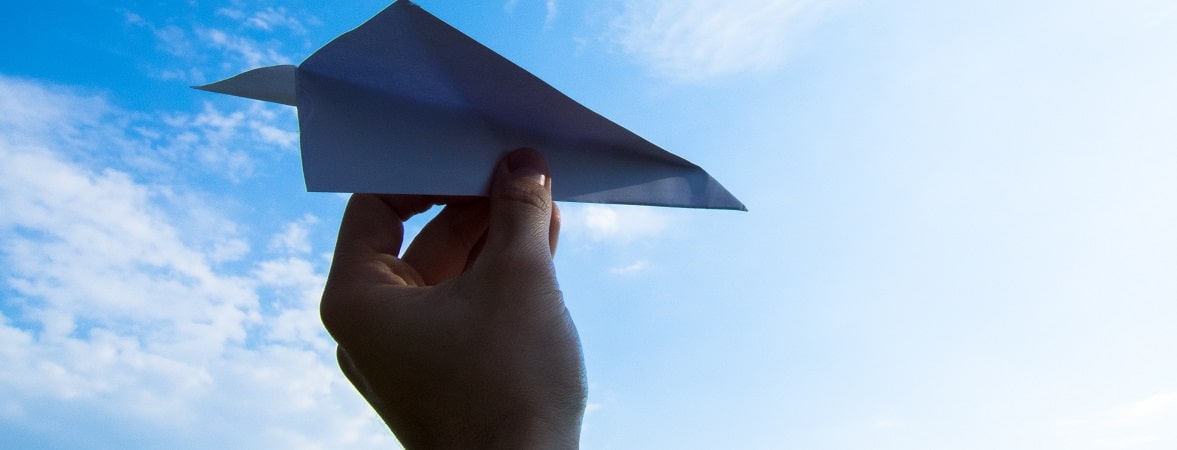 Hand holding paper plane in blue sky